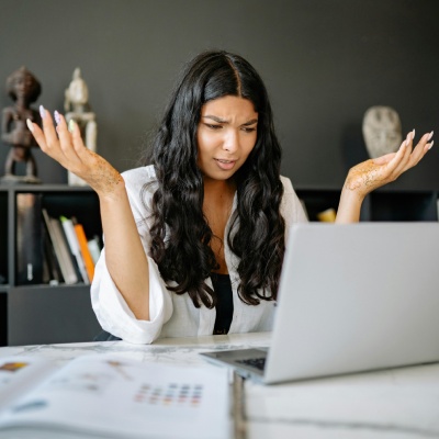Person with hands raised and frowning looking confused at the laptop in front of her. Do you need financial and legal costing help?